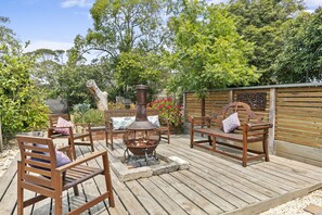 An outdoor patio with wooden furniture, a fire pit, and a wooden fence. - The Beach House Anglesea (Anglesea)