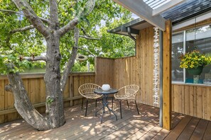 A wooden deck with two wicker chairs and a table, a tree, and a wooden fence.