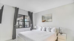 A modern bedroom with a large bed, a nightstand, a window with curtains, and a wall-mounted artwork. - CLOSE TO UNIVERSAL and International drive, 2 bedroom king suite with parking (Orlando)