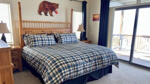 Una camera da letto con una testiera in legno, un letto grande con copripiumino a quadri, un comodino con una lampada e una decorazione a parete con un orso.