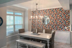 A dining area with a white table, wicker chairs, and a chandelier. - Steps to Sand: Hilton Head Retreat w/ Pool Access! (Hilton Head Island)