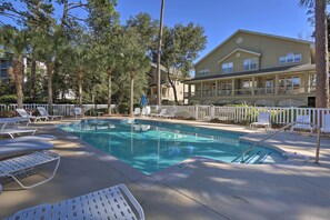A pool area with lounge chairs and a fence, surrounded by trees and a building with balconies. - Steps to Sand: Hilton Head Retreat w/ Pool Access! (Hilton Head Island)