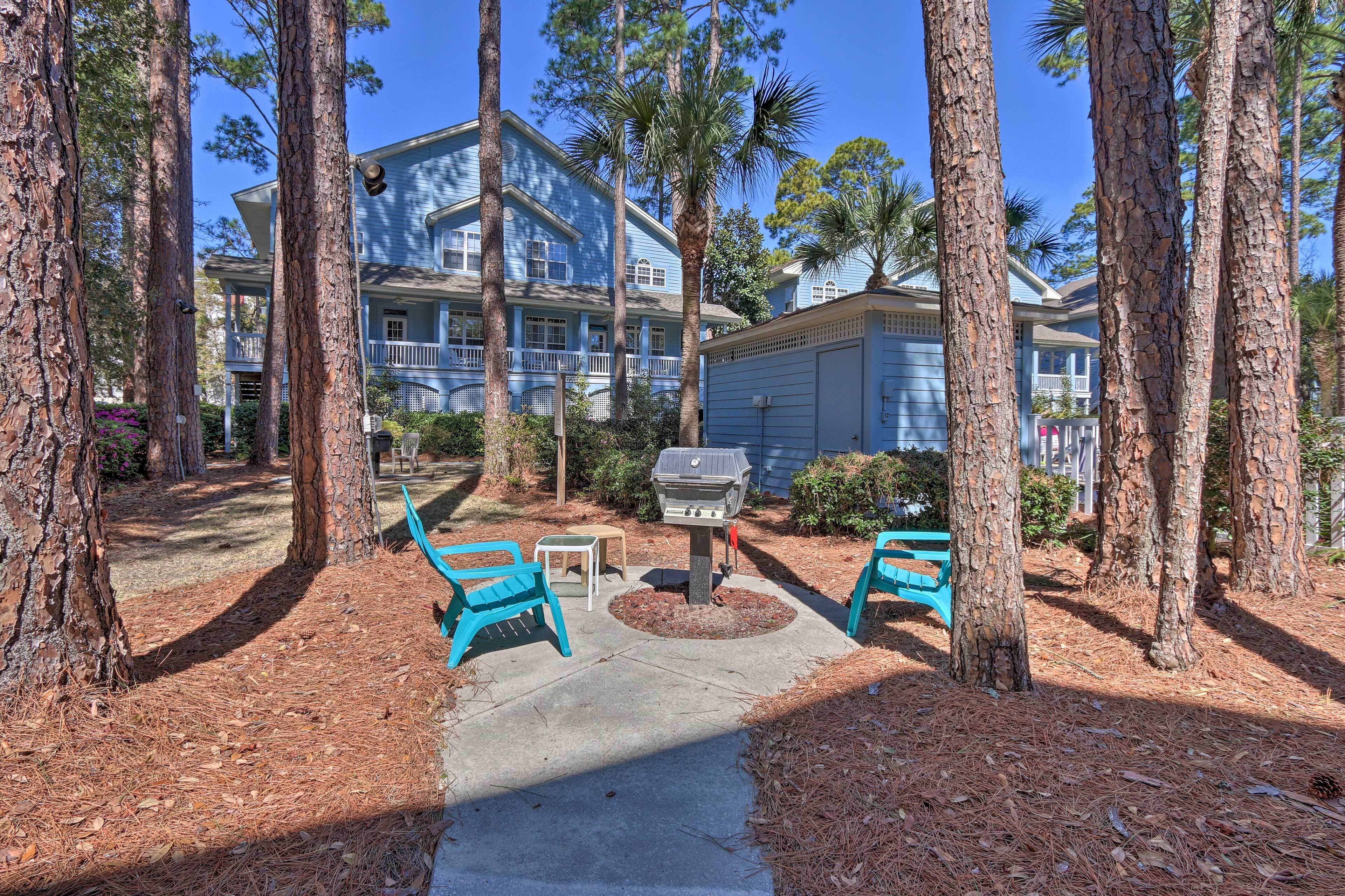 A patio area with two blue chairs, a barbecue grill, and a pathway leading to a building with a blue exterior.