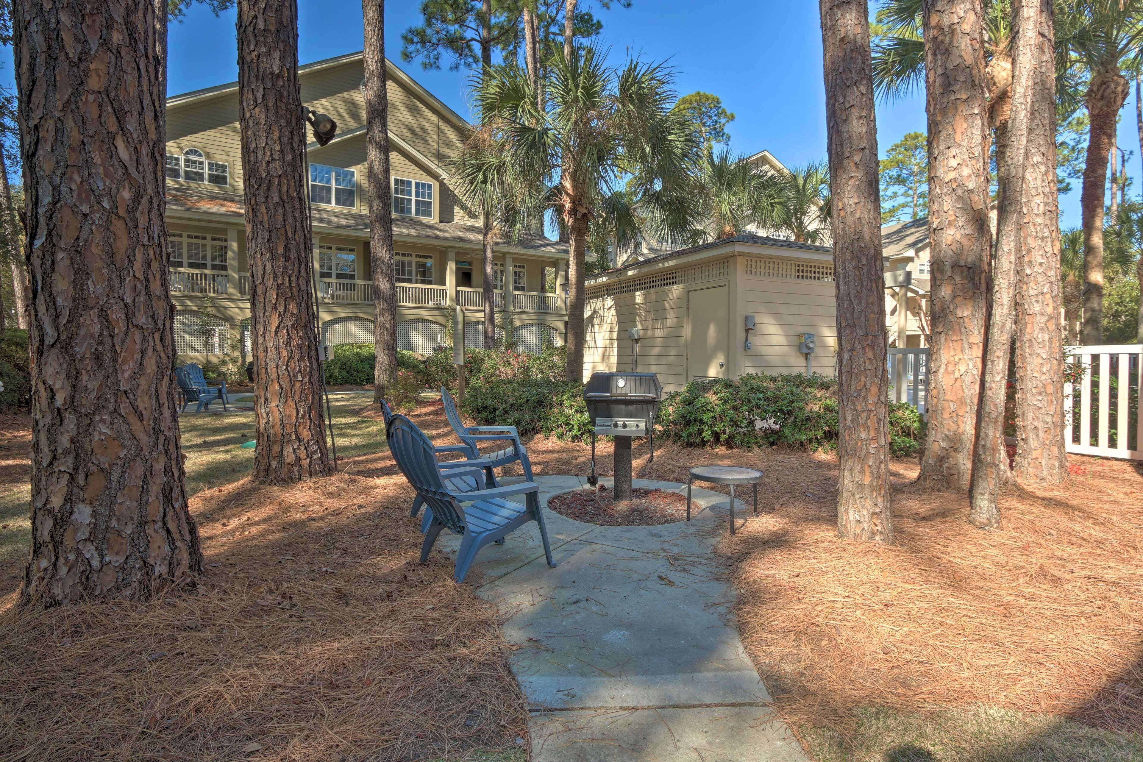 A patio area with a grill, chairs, and a pathway surrounded by trees.