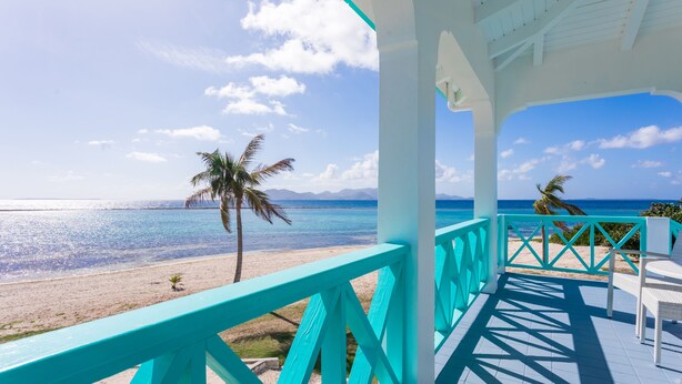 Vue sur la plage depuis un espace abrité, agrémenté de rampes turquoise et de mobilier blanc.