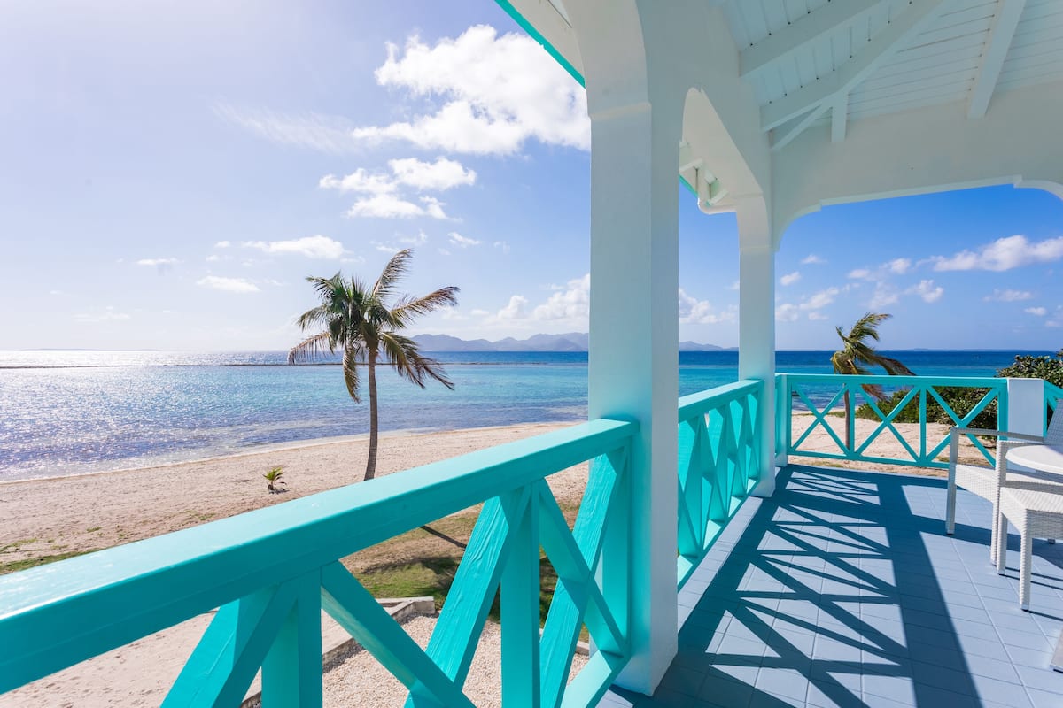 Vue sur la plage depuis un espace abrité, agrémenté de rampes turquoise et de mobilier blanc.