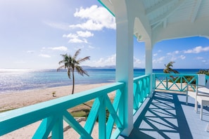 Vistes a la platja des d'una zona protegida, amb baranes turquesa i mobles blancs.