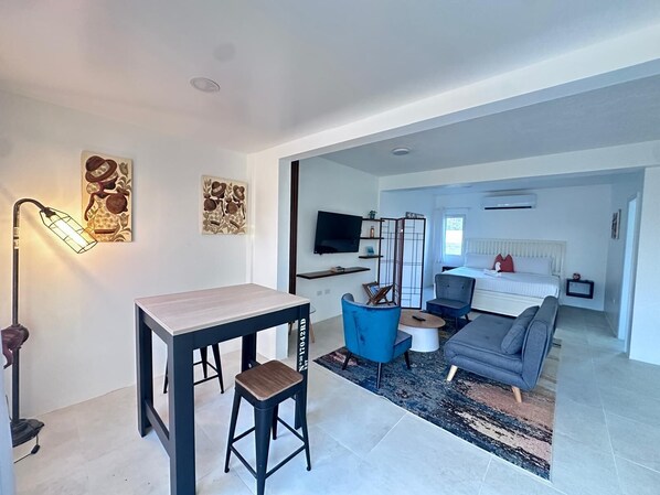 A modern living room with a dining area, a sofa, a TV, and artwork on the walls. - Coralito Bay Suites & Villas (The Valley)