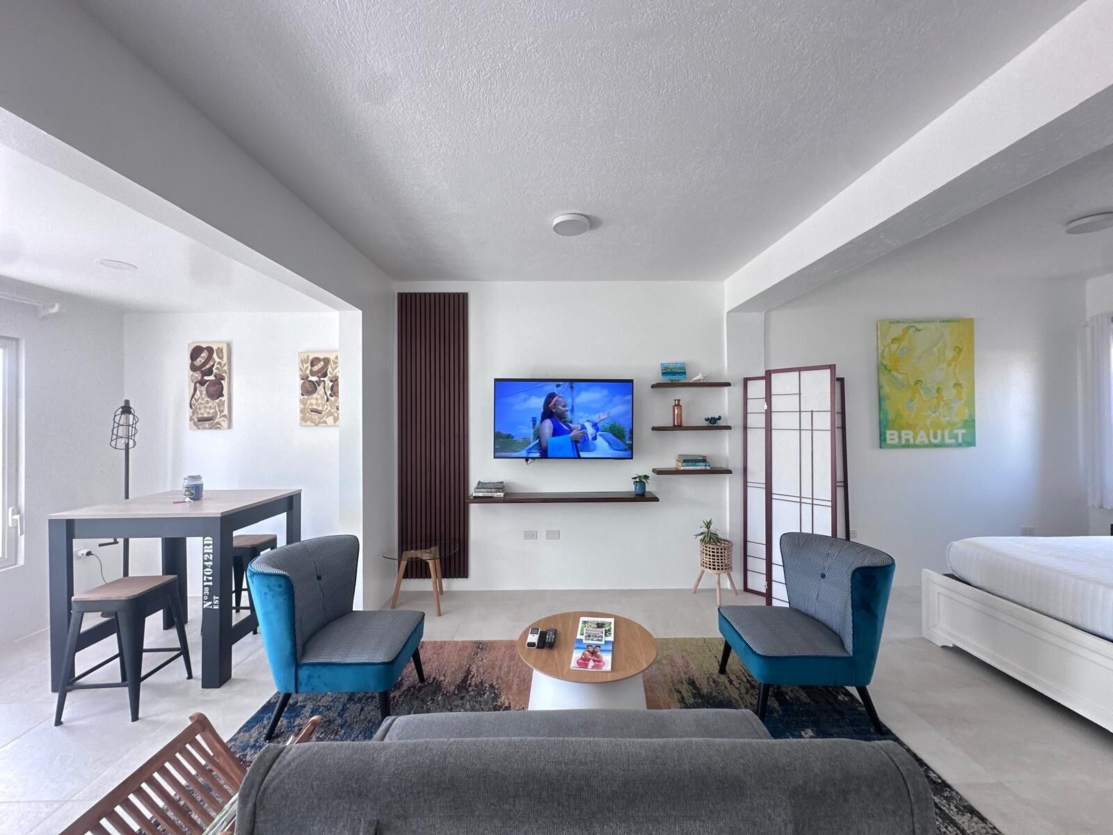 A modern living room with a flat-screen TV, two armchairs, a sofa, a coffee table, and a dining area with a table and chairs.