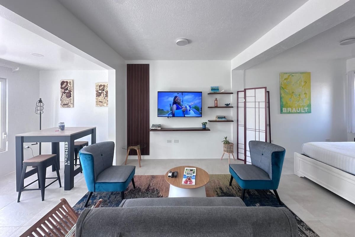 Un salon moderne doté d’un téléviseur à écran plat, de deux fauteuils, d’un canapé, d’une table basse et d’un coin repas avec une table et des chaises.