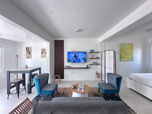 Un salon moderne doté d’un téléviseur à écran plat, de deux fauteuils, d’un canapé, d’une table basse et d’un coin repas avec une table et des chaises.