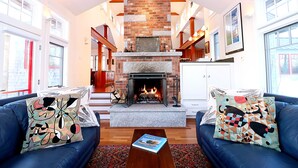 A living room with a fireplace, blue sofas, and patterned cushions. - Super-Private Dream House with Sunset Views (Sedgwick)