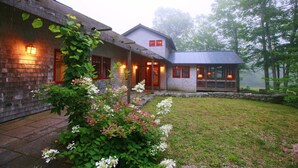 A two-story house with a covered porch, a stone pathway, and a garden with flowering plants. - Super-Private Dream House with Sunset Views (Sedgwick)