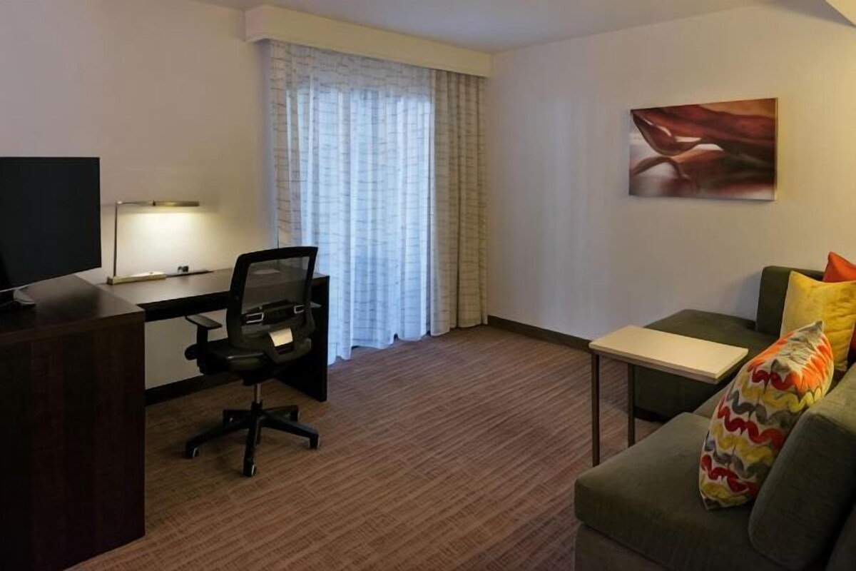 Habitación de hotel con escritorio, silla, sofá y un cuadro en la pared.