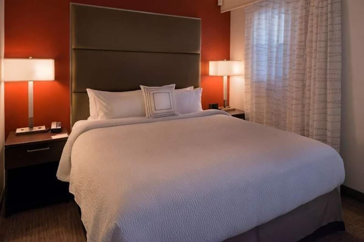 A hotel room with a large bed, two bedside tables with lamps, and a window with curtains.