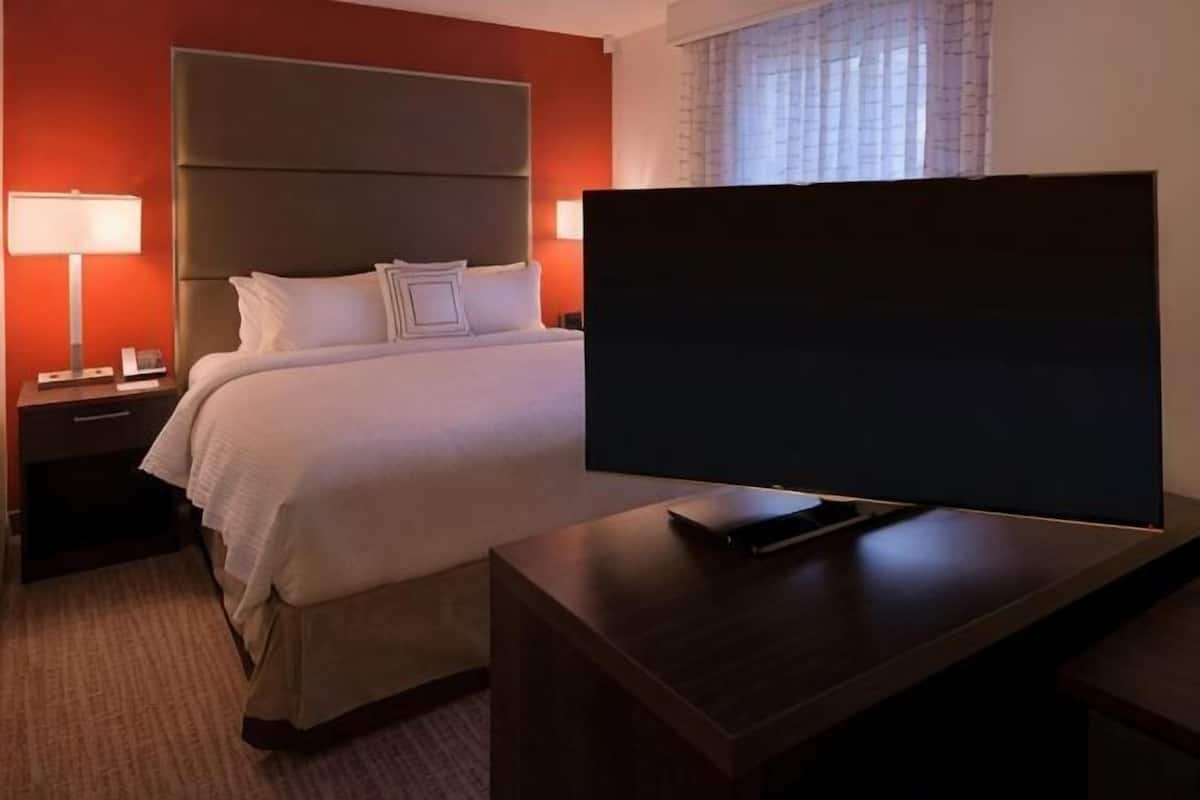 A hotel room with a bed, a television on a stand, a nightstand, and a lamp.