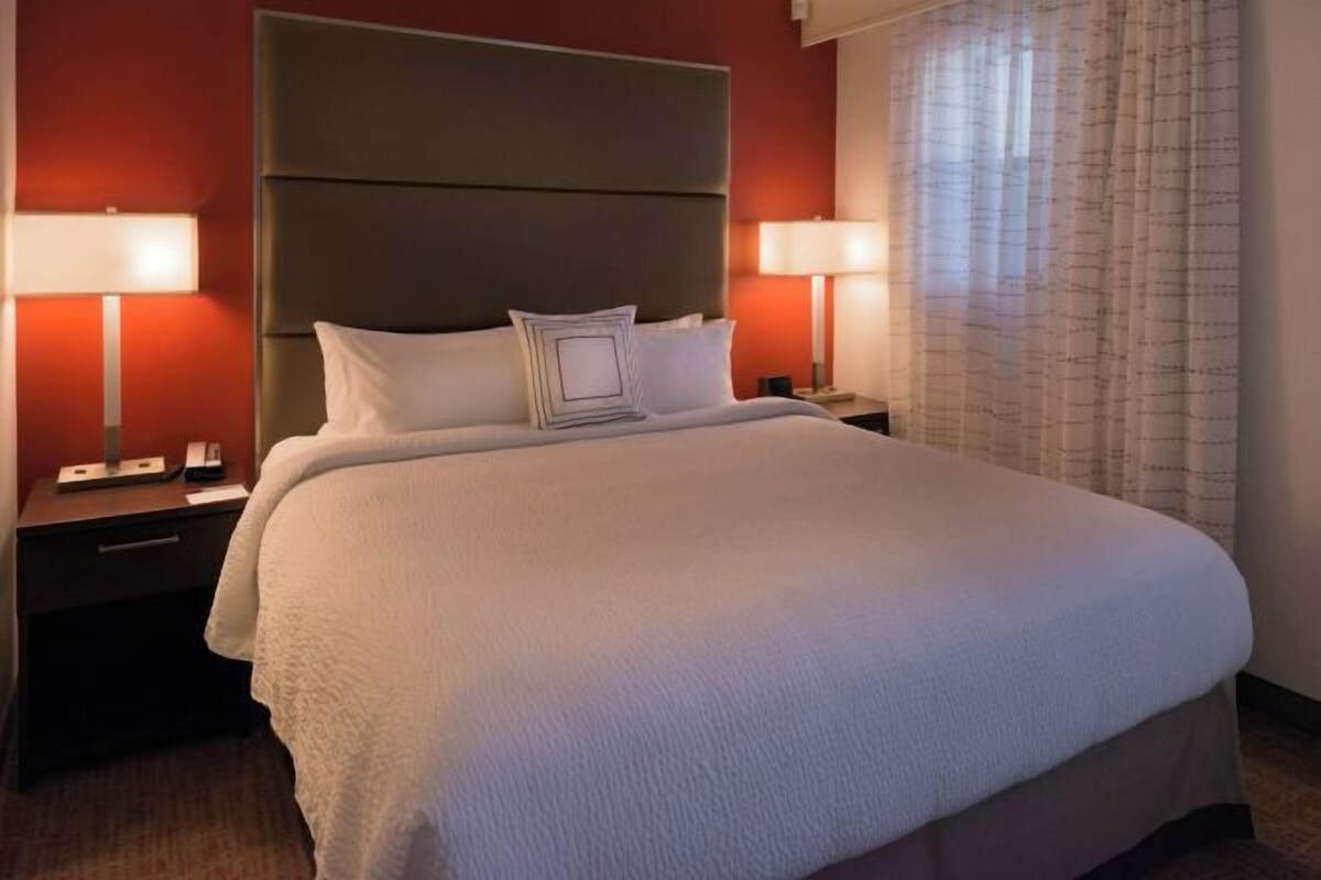 Una habitación de hotel con una cama grande, dos mesitas de noche y un cabecero.
