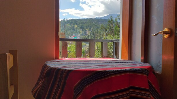 A room with a balcony, a bed with a striped blanket, and a view of a mountainous landscape. - Habitaciones Confortables, Cama Extragrande (Huaraz)