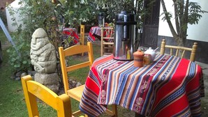 A wooden table with a colorful striped tablecloth, a stone statue, and a metal kettle. - Habitaciones Confortables, Cama Extragrande (Huaraz)