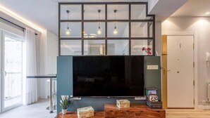 Un salon doté d’un grand téléviseur à écran plat fixé sur un meuble en bois, d’une cloison en verre au-dessus du téléviseur et d’une porte située à droite.