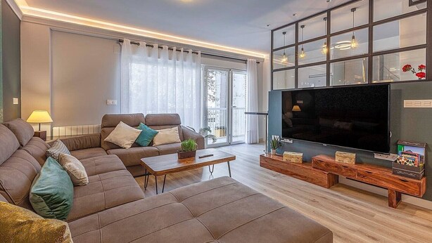 Un salon moderne avec un canapé d’angle, un téléviseur à écran plat et une table basse en bois.