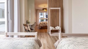 Une chambre d’hôtel moderne avec un plancher en bois, un bureau avec une chaise, un lit recouvert d’une courtepointe à motifs et une armoire en bois contenant des serviettes.