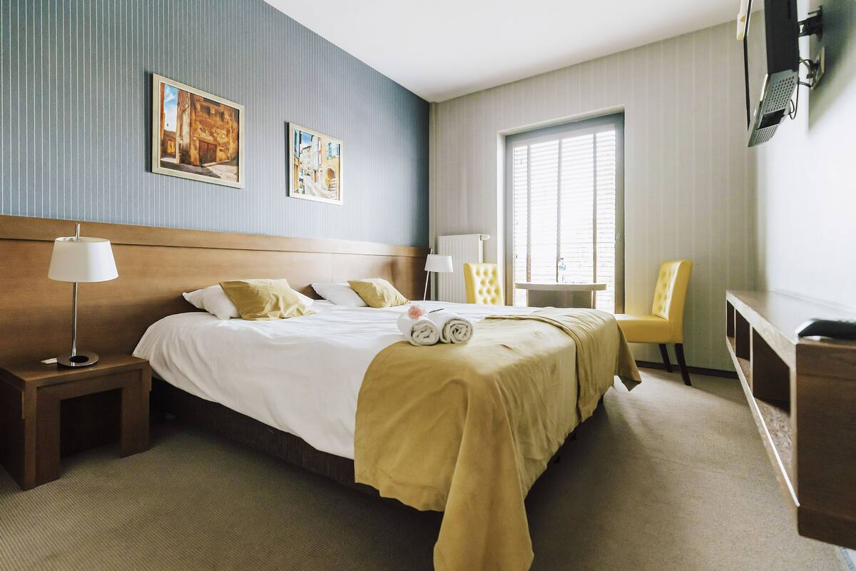 Habitación de hotel con una cama grande, una mesita de noche, una silla, un escritorio y una ventana con persianas.