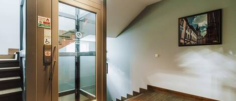 Un ascenseur moderne avec des portes en verre, un escalier et un tableau accroché au mur.