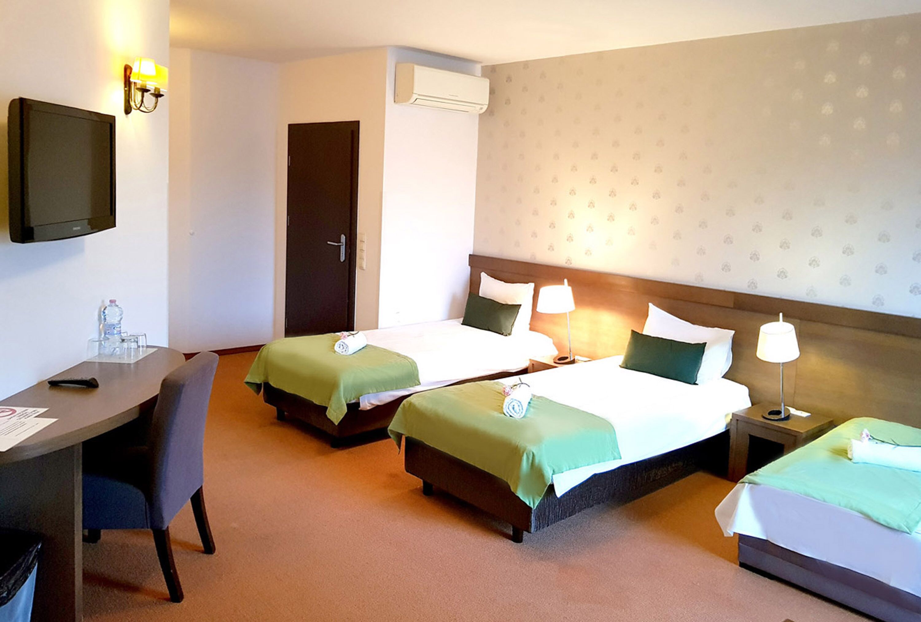 A hotel room with two beds, a desk, a chair, a TV, and a lamp.