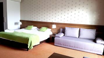 A hotel room with a bed, a sofa, a nightstand, and a wall-mounted air conditioner.