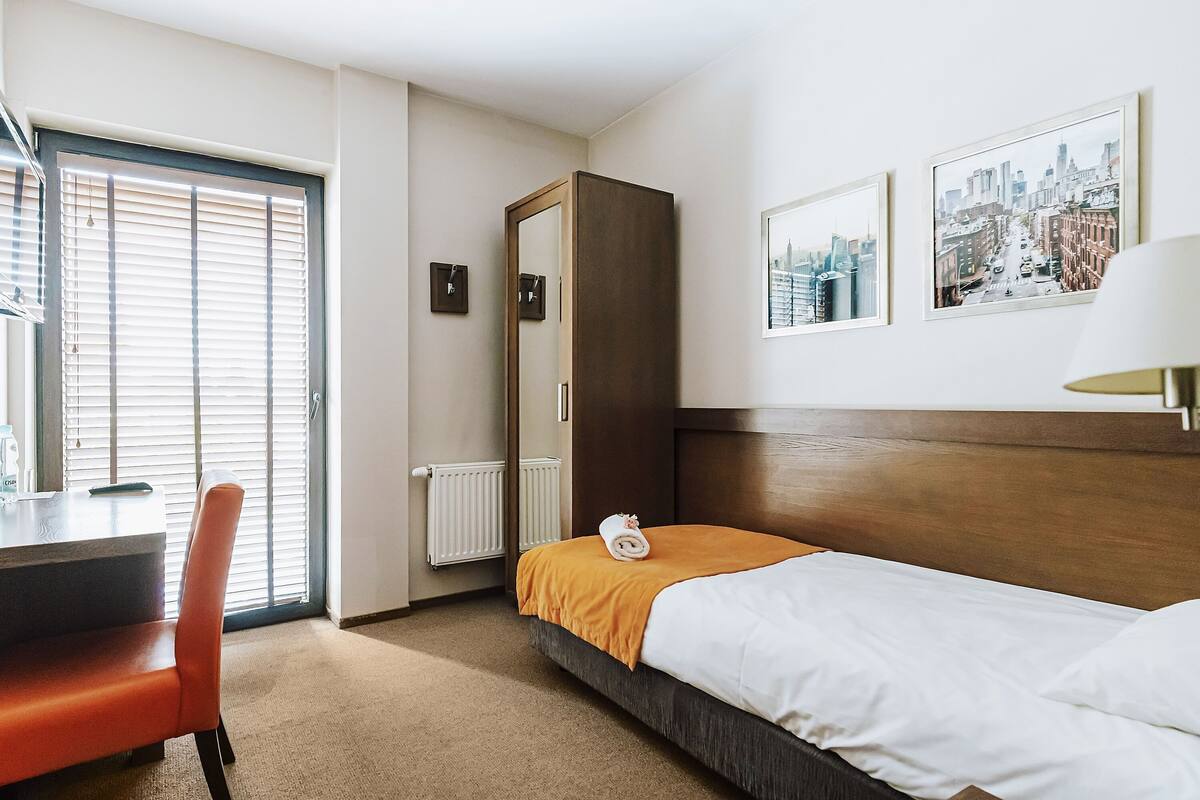 Una habitación de hotel con cama, escritorio, silla, espejo y dos cuadros en la pared.