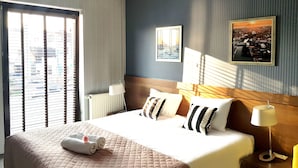 Una habitación de hotel con una cama grande, una mesita de noche, una lámpara y una ventana con persianas.