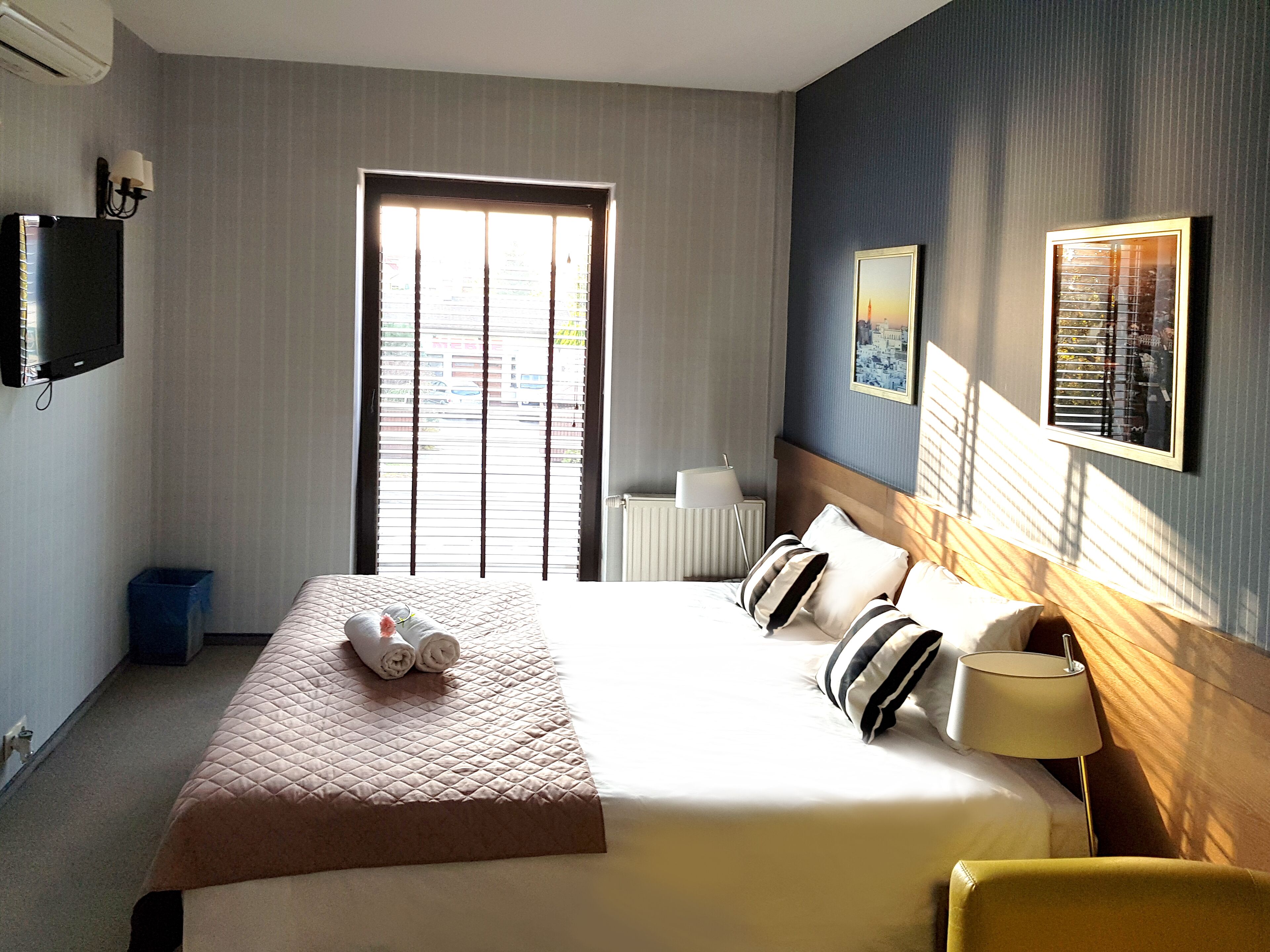 Une chambre d’hôtel avec un grand lit, une lampe de chevet, un téléviseur et une fenêtre avec des stores.