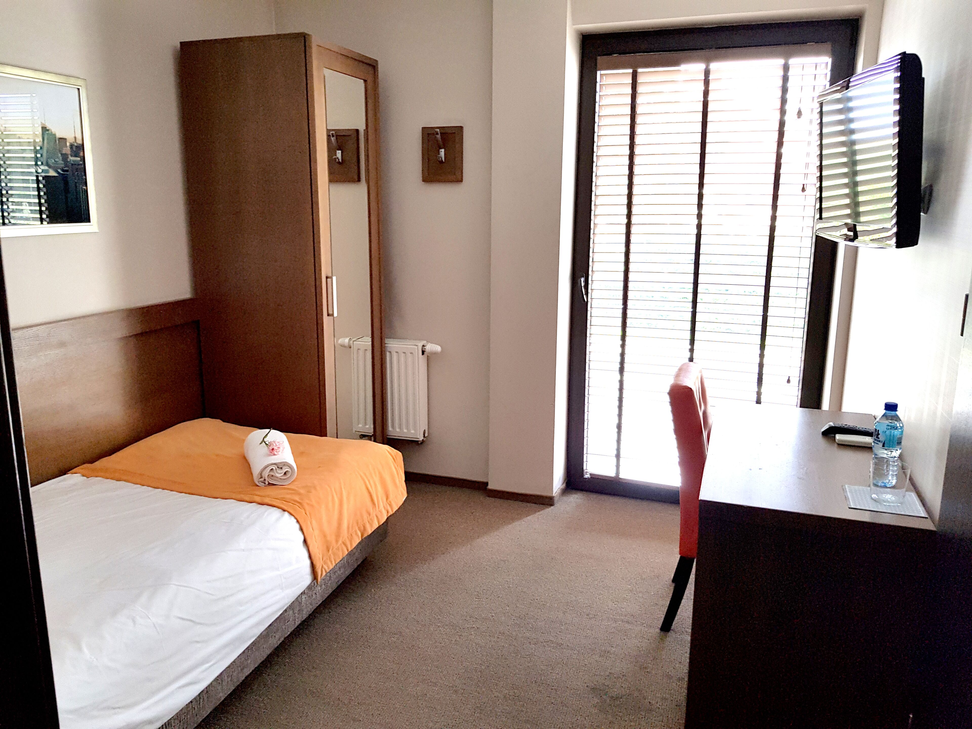 Una habitación de hotel con cama, escritorio, silla, radiador y ventana con persianas.