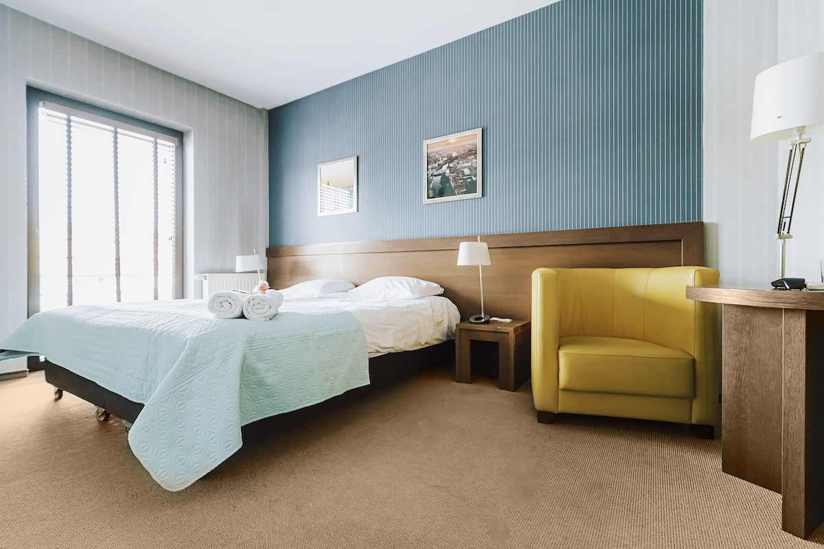 Una habitación de hotel con una cama, una mesita de noche, una lámpara, una silla y un cuadro en la pared.