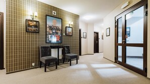 Un vestíbulo de hotel con un mostrador de recepción, dos sillones y un cartel grande que anuncia el hotel.