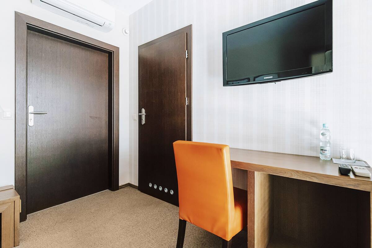 Habitación de hotel con un escritorio de madera, una silla naranja, un televisor montado en la pared y dos puertas.