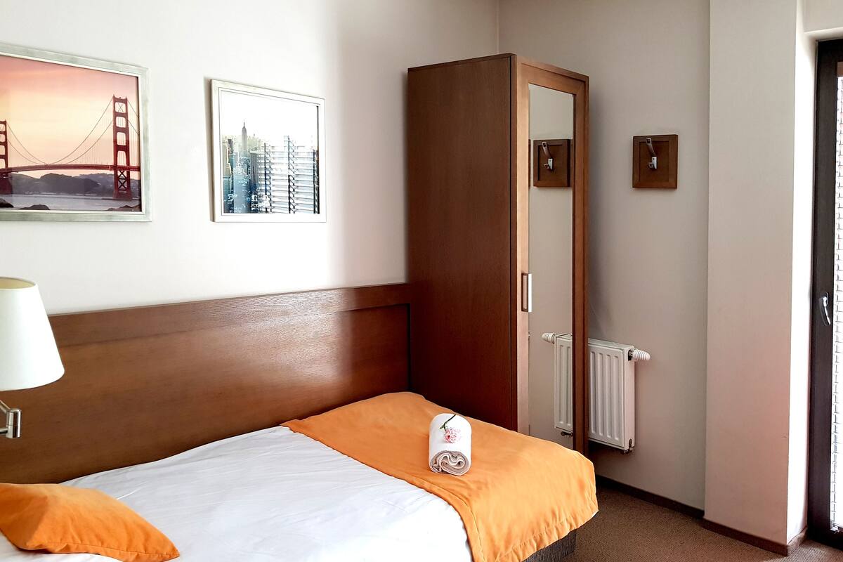 Una habitación de hotel con una cama, un armario de madera, un cuadro con un puente y un radiador.