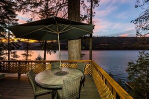 A wooden deck with a round table and wicker chairs, overlooking a calm lake at dusk. - Lakefront Cabin with private pier on Donner Lake (Truckee)