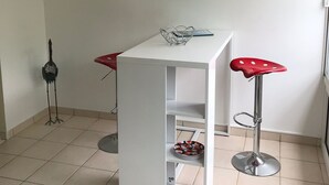 A small, modern room with a white table and two red bar stools. A framed artwork hangs on the wall above the table.