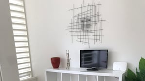 A modern living room with a grey sofa, colorful rug, white shelves, a TV, and a plant.