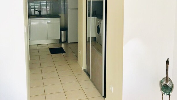 A narrow hallway leading to a kitchen with white cabinets, a microwave, and a washing machine.