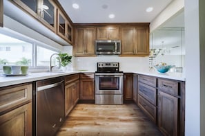 Une cuisine moderne avec des meubles en bois, des appareils électroménagers en acier inoxydable et une fenêtre qui laisse entrer la lumière naturelle.