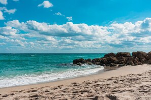 Ein Strand mit klarem türkisblauem Wasser, sandigem Ufer und großen Felsen.