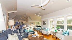 A spacious living room with a large sectional sofa, a round coffee table, and a dining area with a white table and chairs. - Get ready for an unforgettable marsh view at 3 Little Birds on Bald Head Island! (Bald Head Island)
