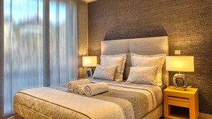 Hotellihuone, jossa on suuri sänky, kaksi yöpöytää valaisimineen, ikkuna verhoineen ja kuvioitu seinä.