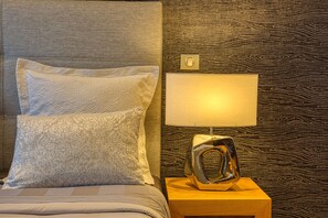 A neatly made bed with patterned pillows, a bedside lamp, and a textured wall.
