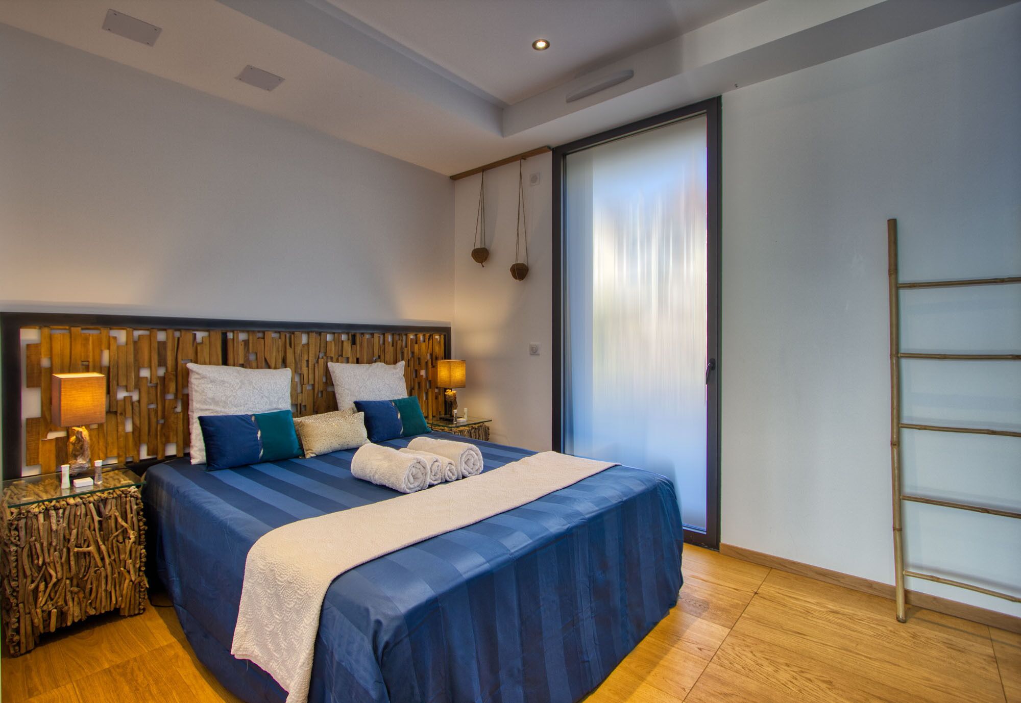 A modern bedroom with a large bed, wooden headboard, bedside lamps, and a sliding glass door.