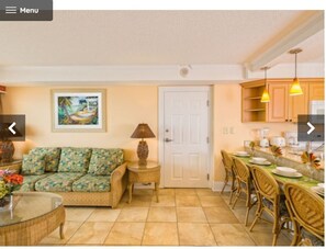 A living room with a sofa, a small table with a lamp, a painting on the wall, and a dining area with chairs and a table. - Westgate Myrtle Beach waterfront (Myrtle Beach)