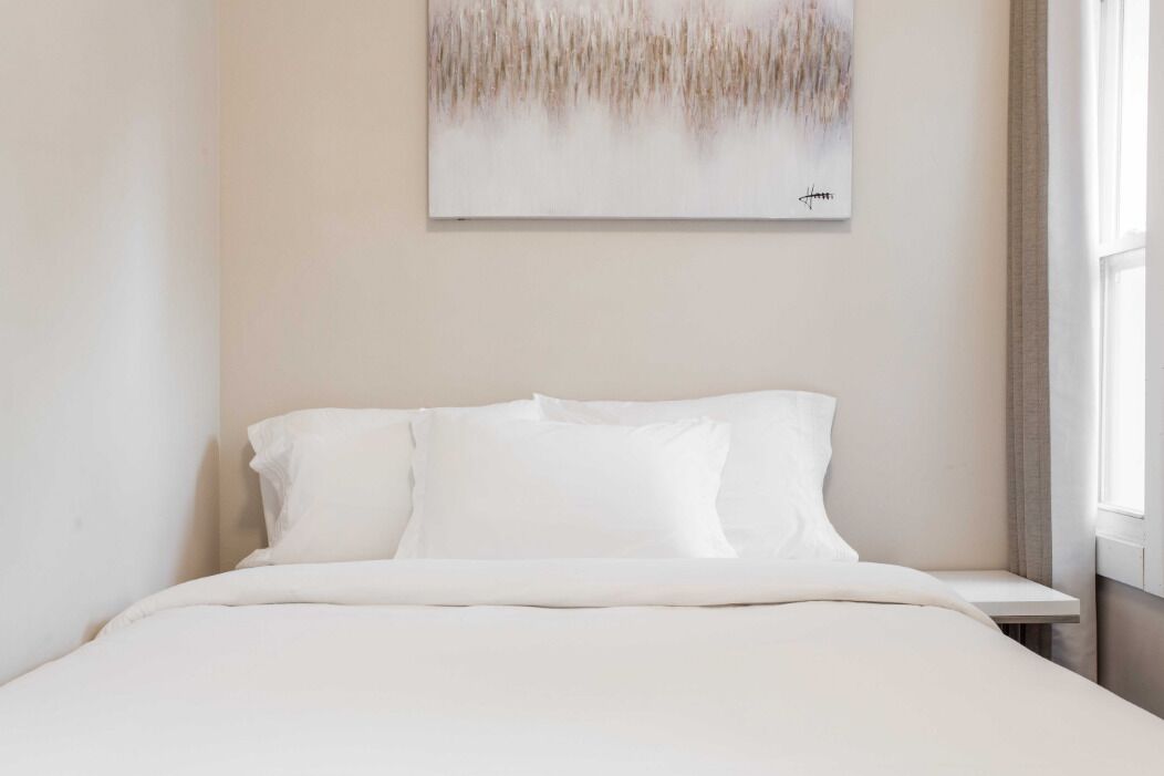 Ein Schlafzimmer mit einem Bett, weißer Bettwäsche, einem Nachttisch und einem Bild an der Wand.